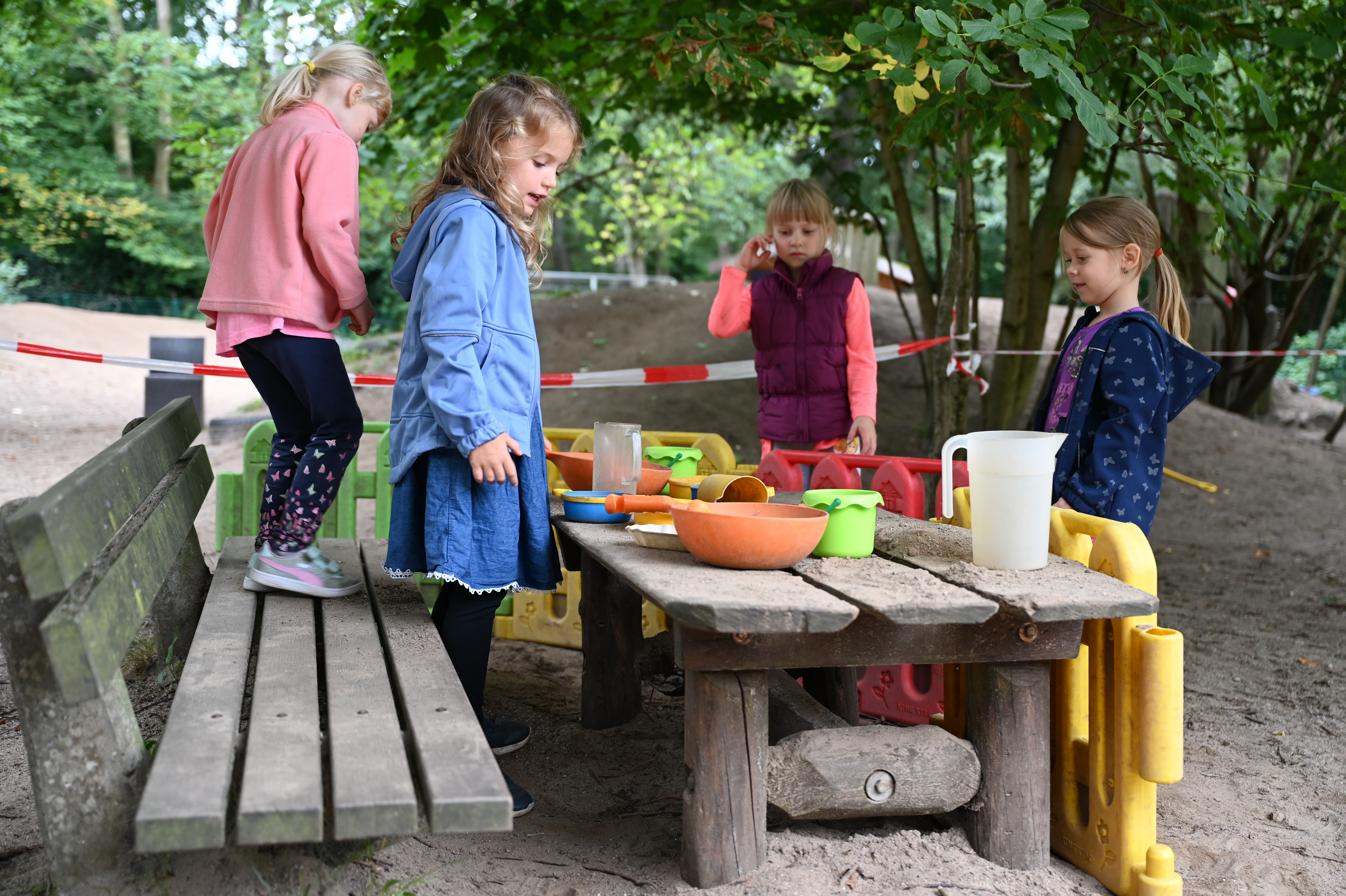 Vier vierjährige Kinder spielen mit Sandspielzeug an einem Holztisch.